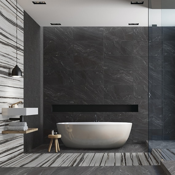Stunning wet room with free-standing bathtub, shower wall, floor, and niche of black marble look tile with white & black tile accents, black matte shower fixtures, floating vanity countertop & shelf.
