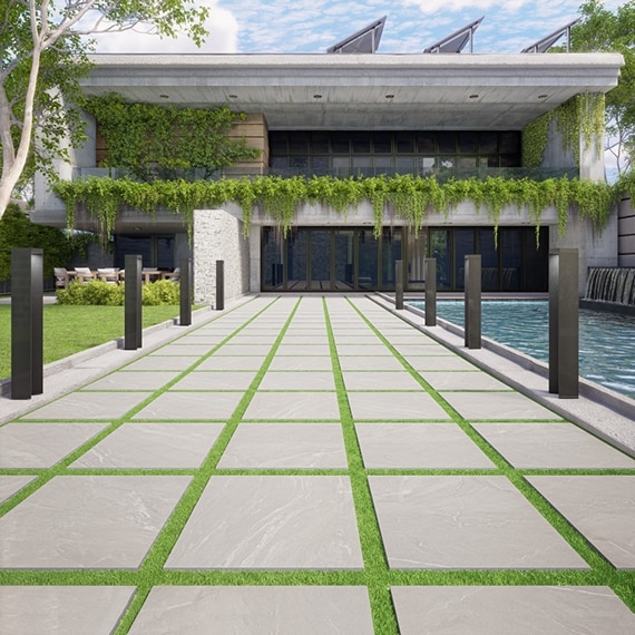 Two-story office building entrance with gray stone-look porcelain pavers set in green turf, waterfall fountain, glass front doors, and balcony lined with hanging vines.