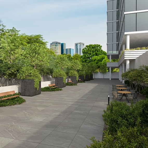 Office building courtyard with gray porcelain pavers that look like stone, dining table & chairs, wooden benches and large planters along white retaining wall. 
