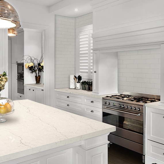 Fresh and clean kitchen décor with white subway tile backsplash, white quartz countertop & island, stainless steel gas stove, and white cabinets.