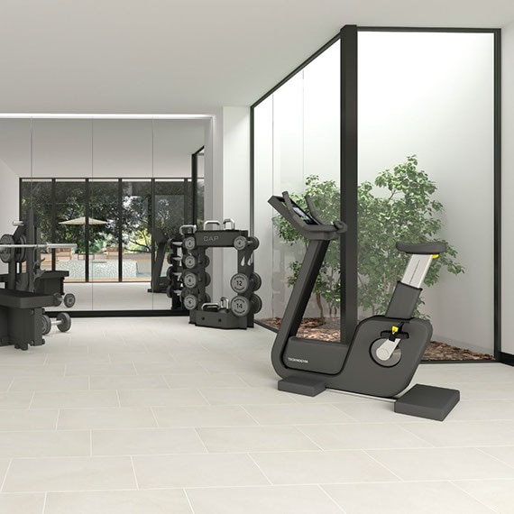 Home gym with cycling machine, free weights, mirrored wall, and off-white floor tile that looks like stone.