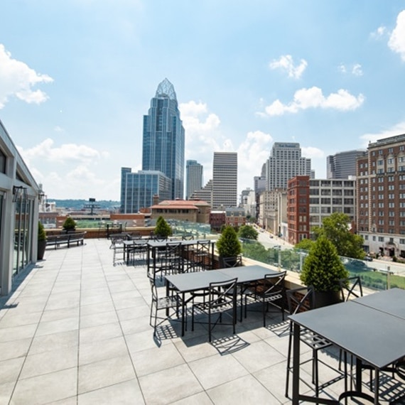 Rooftop restaurant with light beige limestone look 2CM porcelain pavers under black tables & chair with skyscrapers and blue skies in the background.