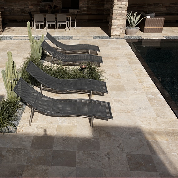 Rustic pool with tan travertine natural stone deck, black lounge chairs, aloe, saguaro and senita cactus.