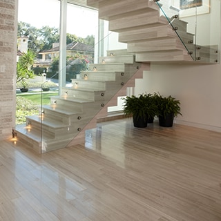 Staircase with wood look tile and glass railings in front of a large floor to ceiling picture window.