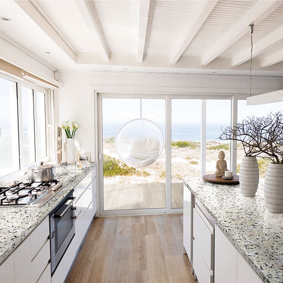 Kitchen countertops & island of white granite with black & tan mineral deposits, patio doors with view of beach and ocean.
