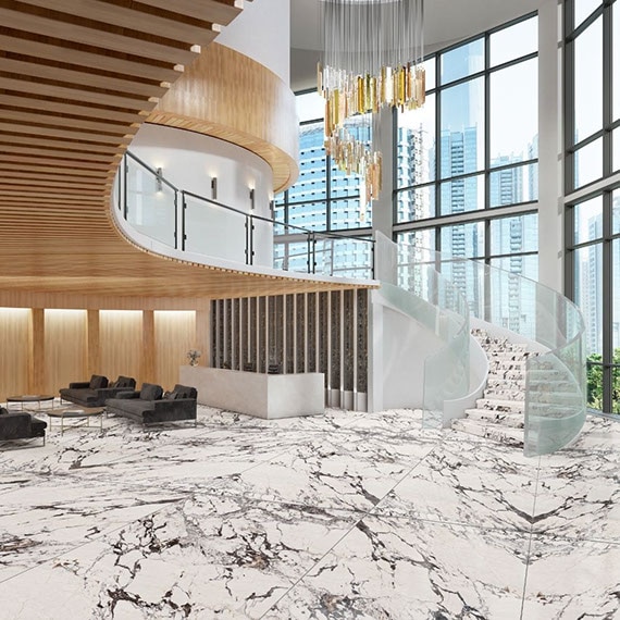 Hotel lobby with marble look, white and brown veined, porcelain slab covering the floor and grand staircase, chandelier, and 2 story windows with view of city skyline.