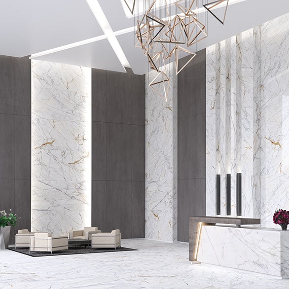 Commercial lobby with tall ceilings, seating area, and front desk. Walls and floors covered in Panoramic Porcelain Surfaces in white marble look slab.