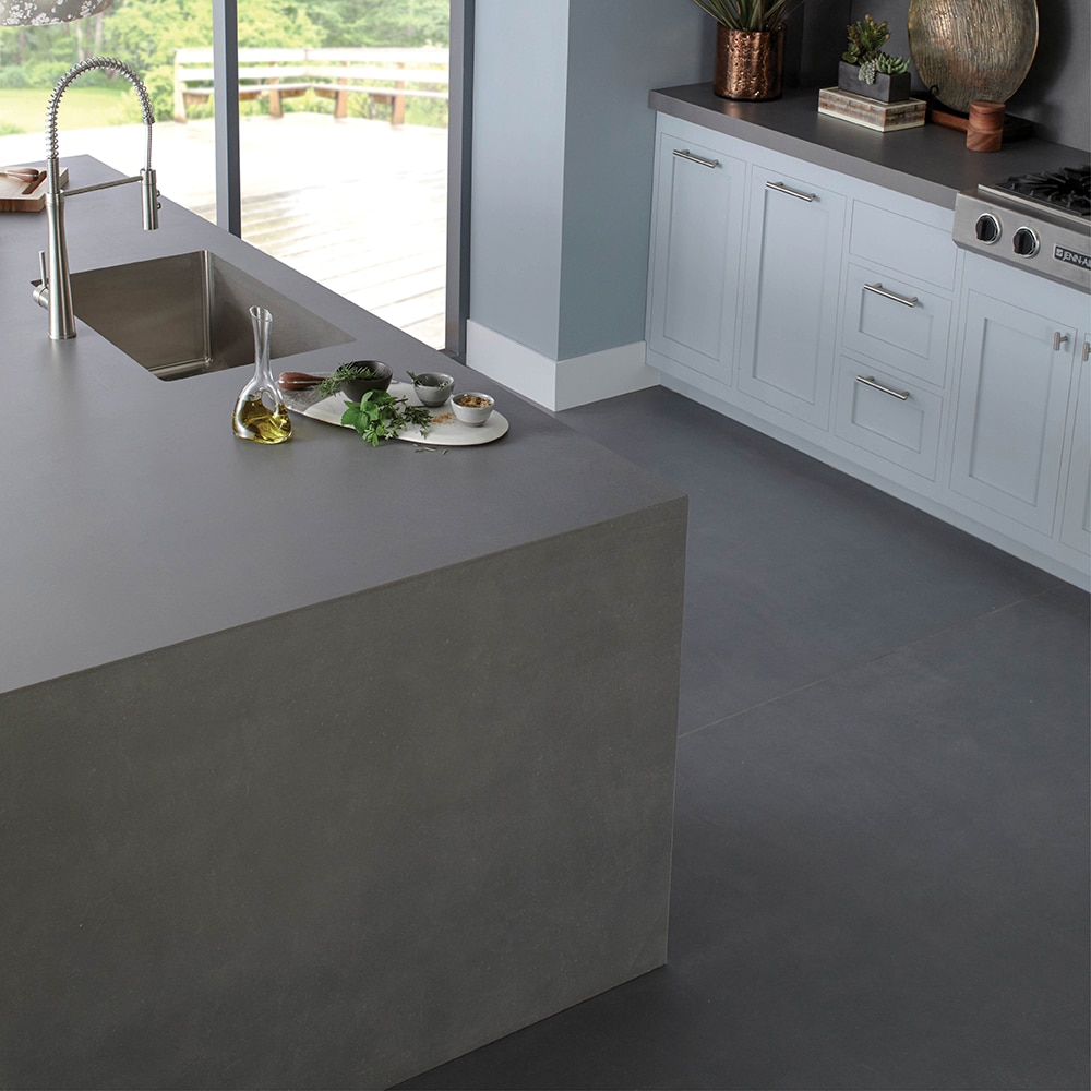 Kitchen with white cabinets, gray slab countertop, gray slab waterfall style center island, and gray concrete look floors.