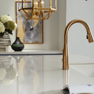 Closeup of white glossy countertop made from large format porcelain slab, brushed brass faucet, and brushed brass caged pendant light.