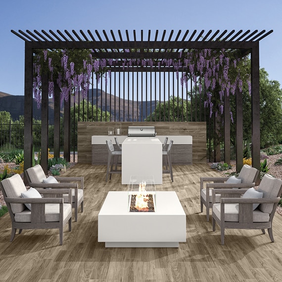 Outdoor patio / kitchen with floor tiles that look like wood, white porcelain slab island and firepit, stainless steel grill, and lavender hanging from pergola.