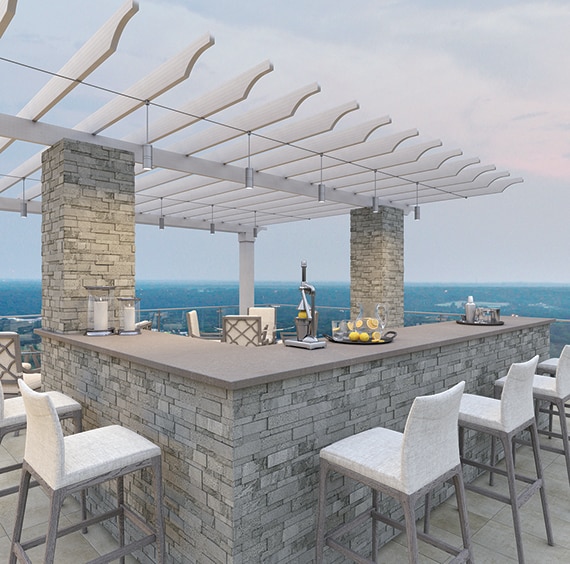 Rooftop patio with gray porcelain slab countertops, gray stacked stone-faced bar under a pergola, white linen bar stools, and wood look floor tile.