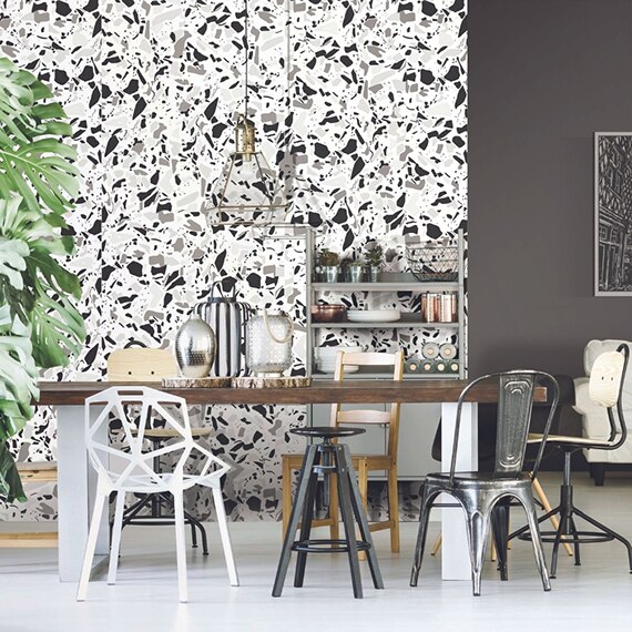 Open living room and dining room with feature wall made of white, gray, and black terrazzo look porcelain slab, table with mismatched chairs, and white sofa.