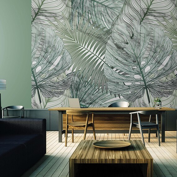 Lobby with tall feature wall with large green tropical leaves on porcelain slab, woodgrain desk with chair, laptop, and side chairs, black couch with wood coffee table.