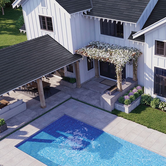 Bird’s eye view of modern farmhouse backyard with covered patio, pool, and flower-covered pergola with gray stone look tile flooring.