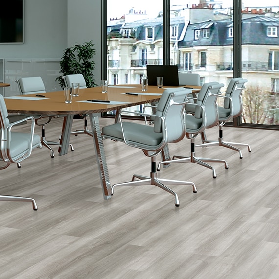 Open concept office with luxury vinyl tile that looks like white oak wood flooring and conference table with pale blue leather rolling chairs.