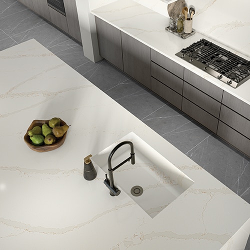 Overhead view of kitchen island sink with white marble slab countertop and gray floors. 