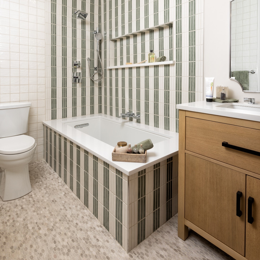 Bathroom showing a full bath and shower with undulated shower tile in a striped pattern alternating between green and white and a white natural stone look oval mosaic on the floor.