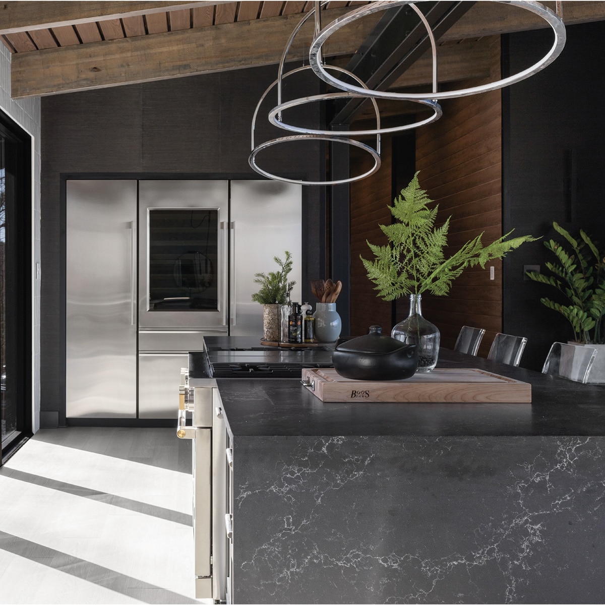 Kitchen with dark wood walls, silver fridge, and center island with a gray marble waterfall countertop.