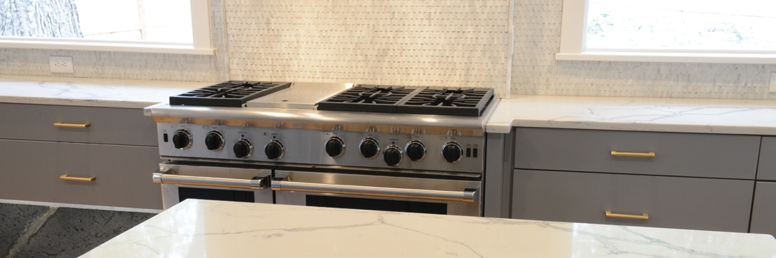 Remodeled kitchen with white with gray veining quartz countertops & island, gray marble mosaic backsplash, stainless steel gas stove/oven.