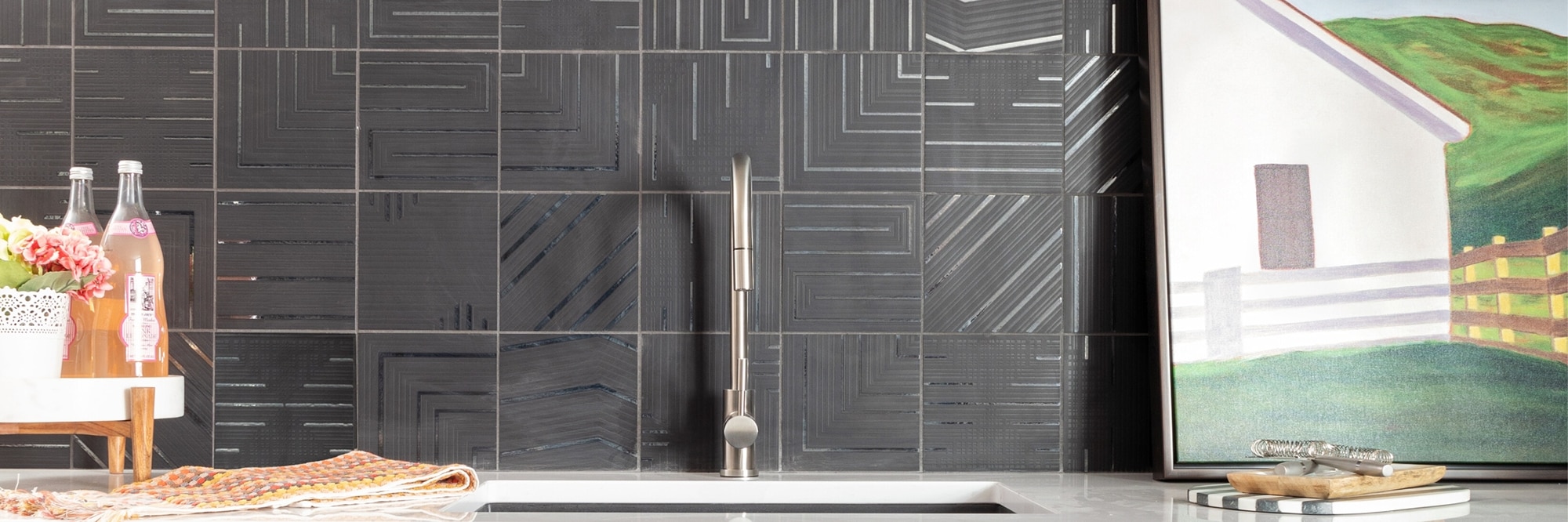 Basement wet bar with black backsplash tile of geometric designs, white quartz countertop, undermount sink with brushed silver faucet.