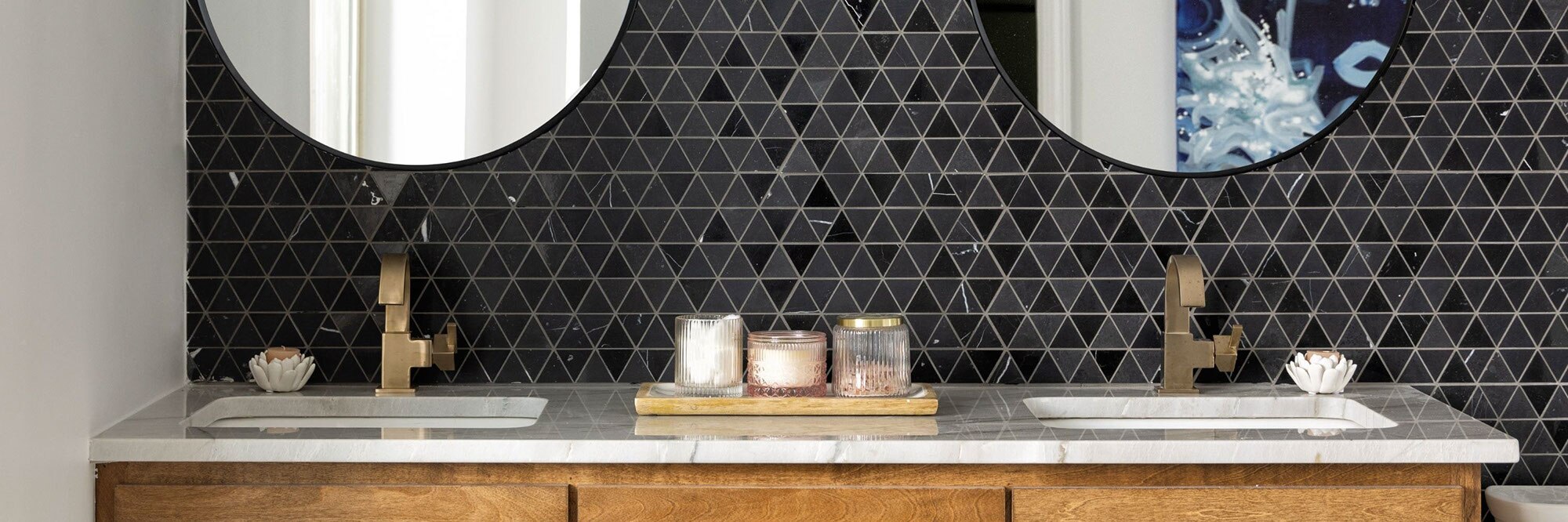Renovated bathroom with woodgrain vanity, gray natural quartzite counter with two sinks, round mirrors on black natural stone triangle mosaic backsplash.