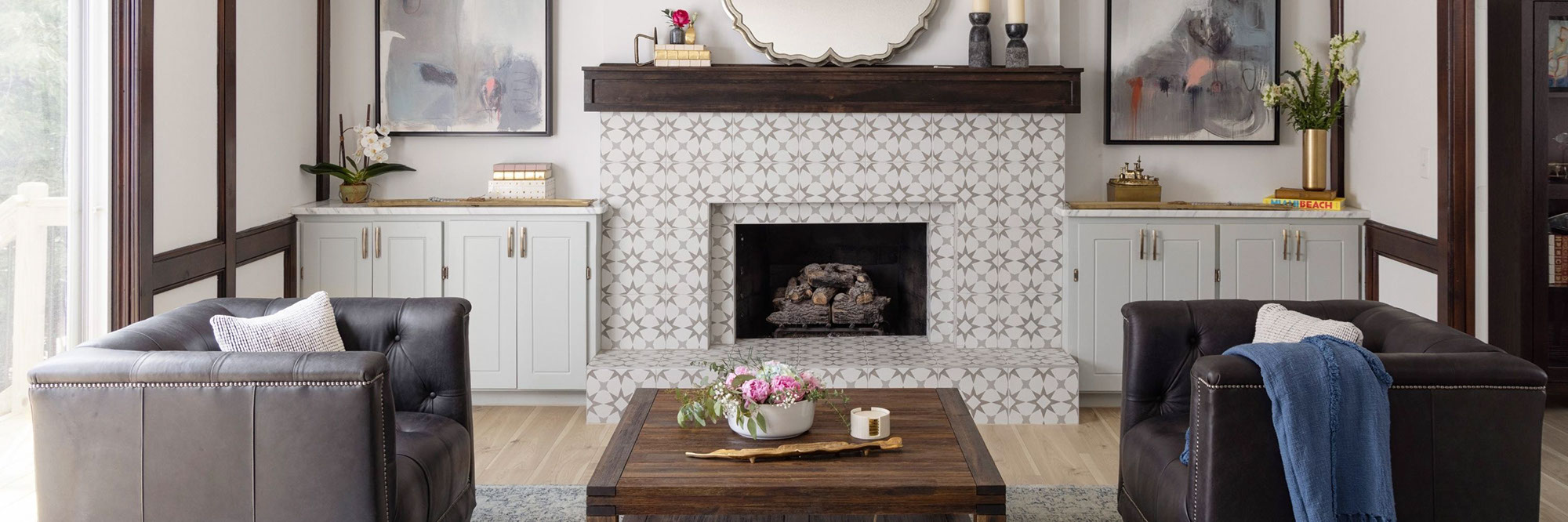 Renovated living room with fireplace façade and hearth of off-white, light gray, and dark gray encaustic tile, dark wood mantel, and off-white built-in cabinets.