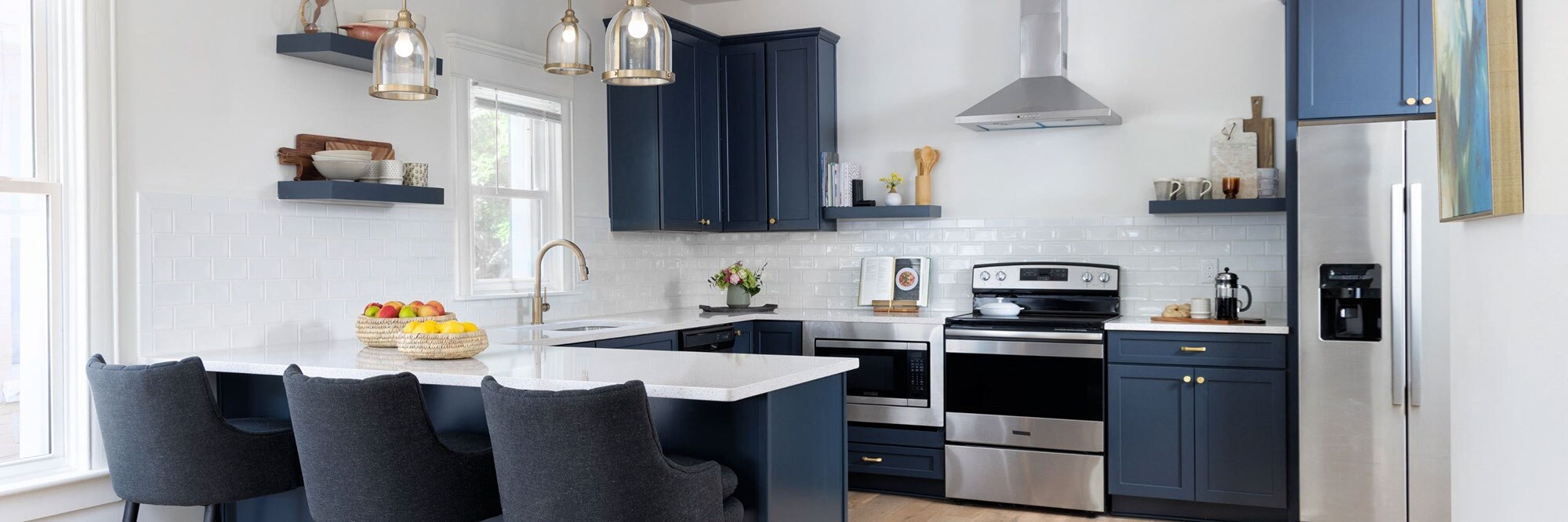 Renovated kitchen with navy cabinets and floating shelves, white glossy subway tile backsplash, white quartz countertops, and stainless steel appliances.