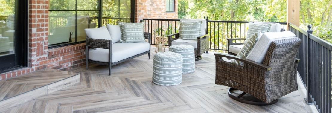 Renovated patio with floor tile that looks like wood plank flooring installed in a herringbone pattern, wicker sofa and chairs with white cushions.