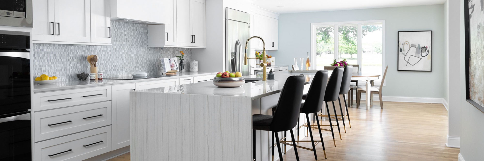 Renovated kitchen with gray natural quartzite countertops and waterfall island, beige & white glass mosaic backsplash, white cabinets and floating shelves.