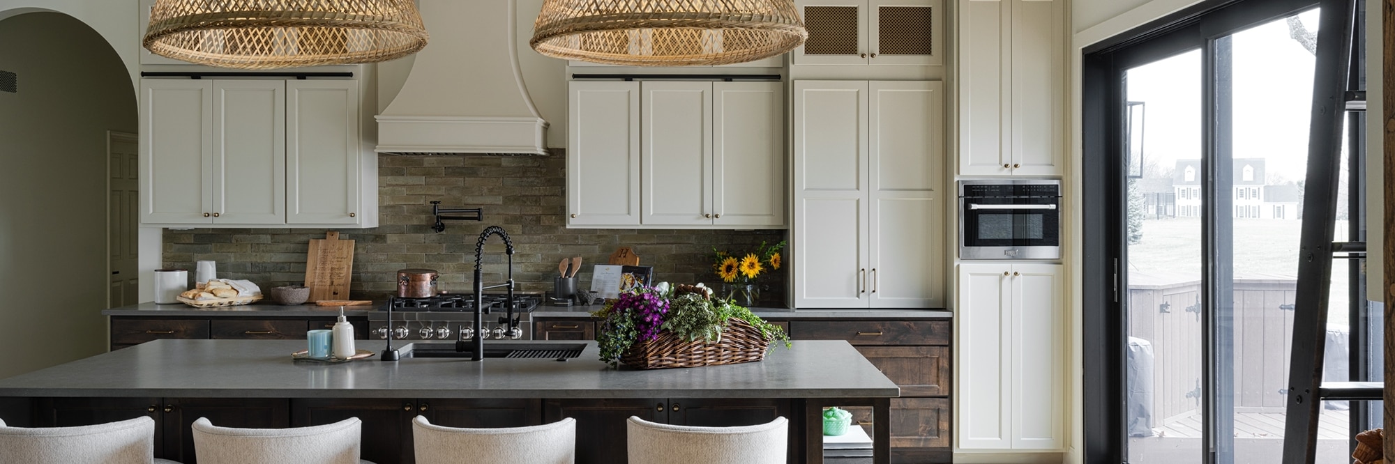 Renovated kitchen with off-white cabinets, glossy brown subway tile backsplash, gray quartz countertops, island with sin and basket pendant lighting.