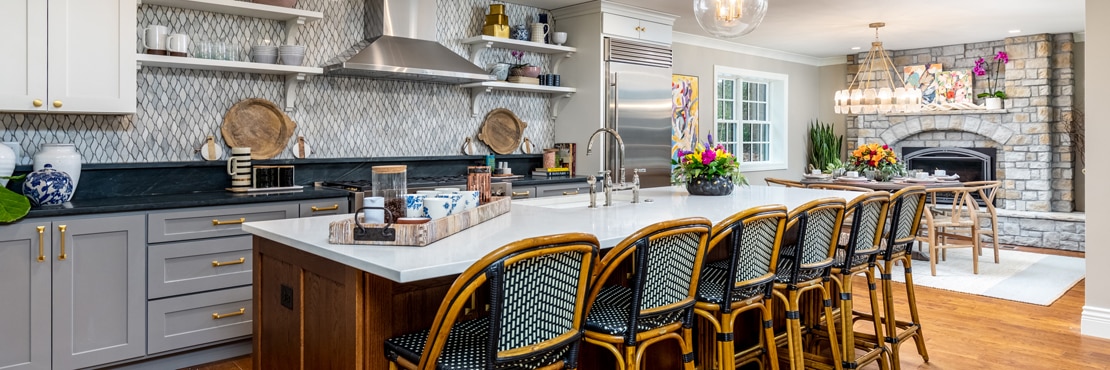 Renovated kitchen with gray marble backsplash tile, black soapstone countertop, island with white quartz countertop and wicker barstools.