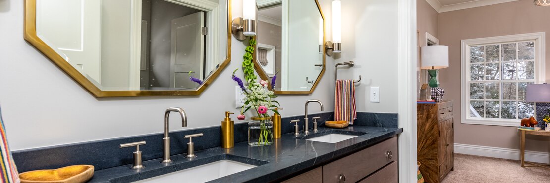 Renovated bathroom with black soapstone vanity counter, dual sinks, dual brass-framed mirrors, and polished brass faucets.