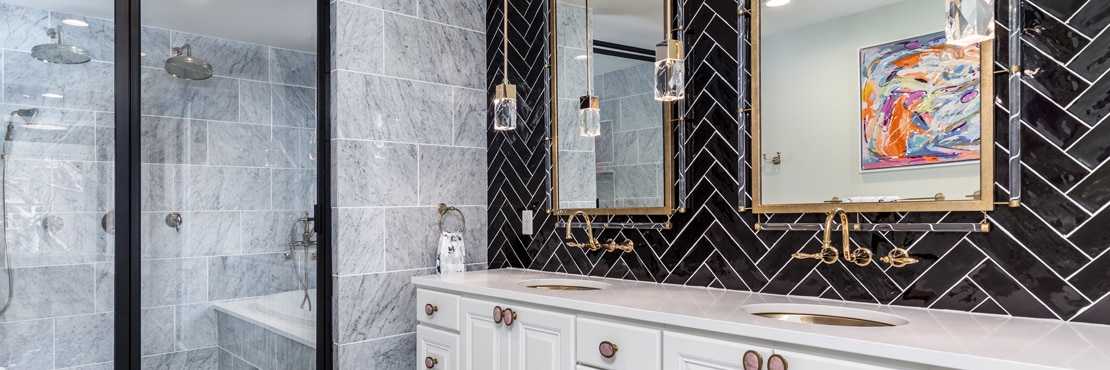 Renovated bathroom with black herringbone tile backsplash, white quart vanity counter with dual sinks, pendant lighting, wet room with marble floor and wall tile.