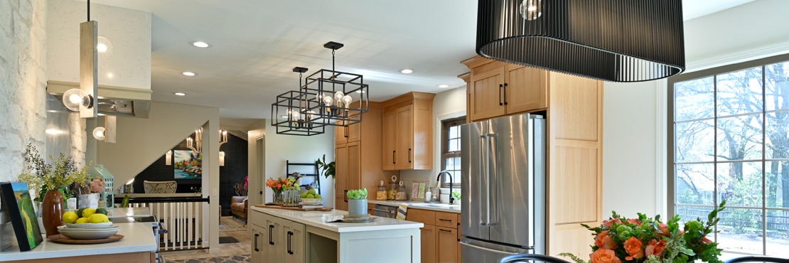 Remodeled kitchen with off-white quartz countertops, wood upper and gray lower cabinets, and black cage pendants over island.