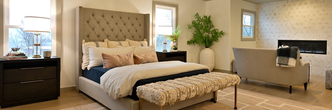 Bedroom with cushioned headboard, nightstands, and wall-mounted fireplace with tan marble and limestone rotating hexagon mosaic wall tile.