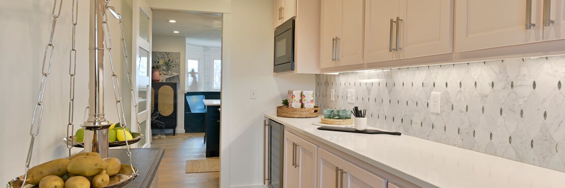 Butler’s pantry with white quartz countertop, white & gray marble mosaic backsplash with antique mirror accents, and white wash wood cabinets.
