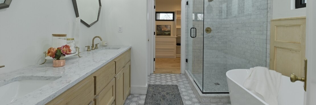 Bathroom with white & gray marble mosaic flooring, marble countertop over natural wood cabinets, shower with marble tile and standalone tub.