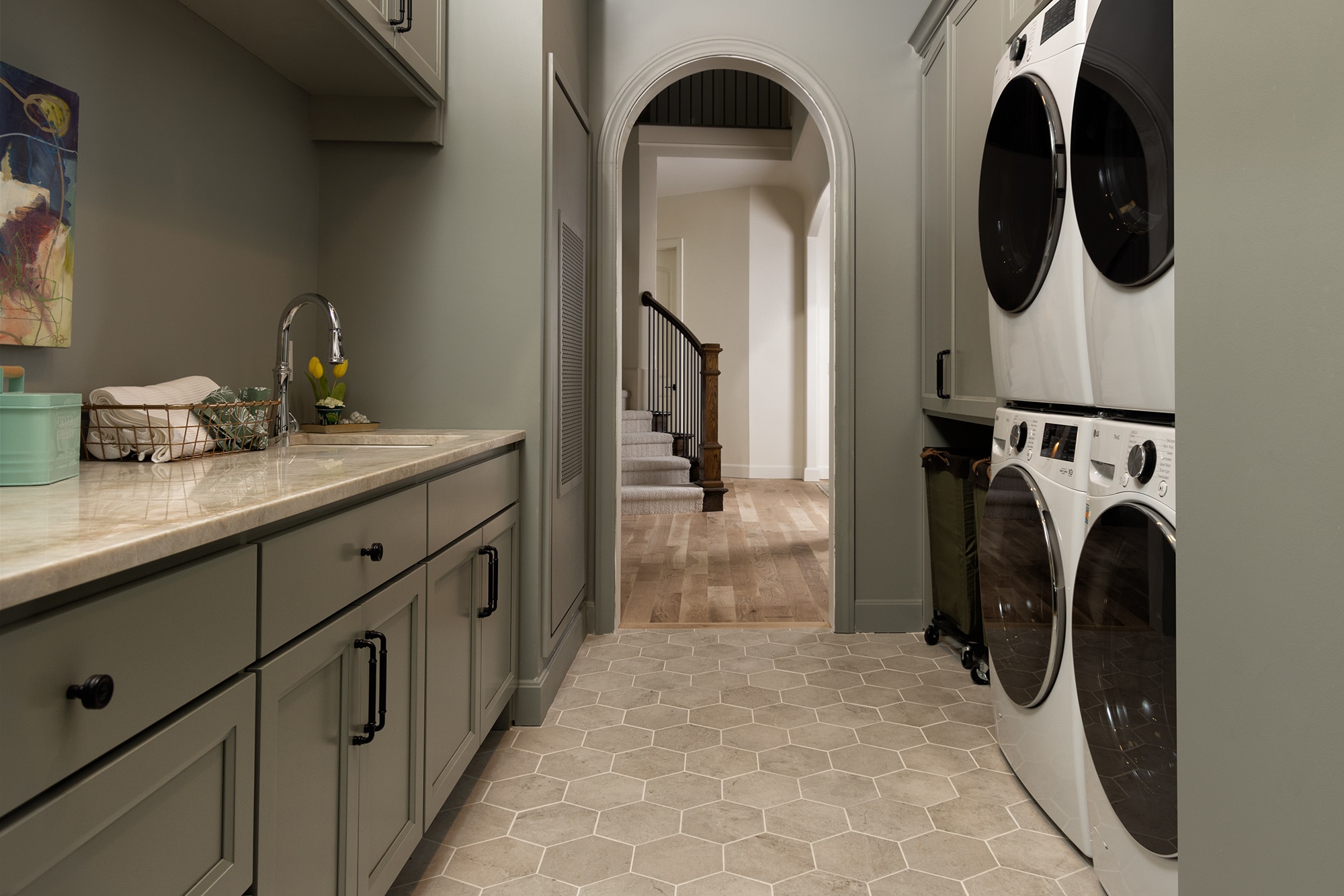 Mudroom with washing sink on left wall and washing machines on right wall. Beige stone look hexagon floor tile and a beige marble look quartzite slab countertop on the washing sink.