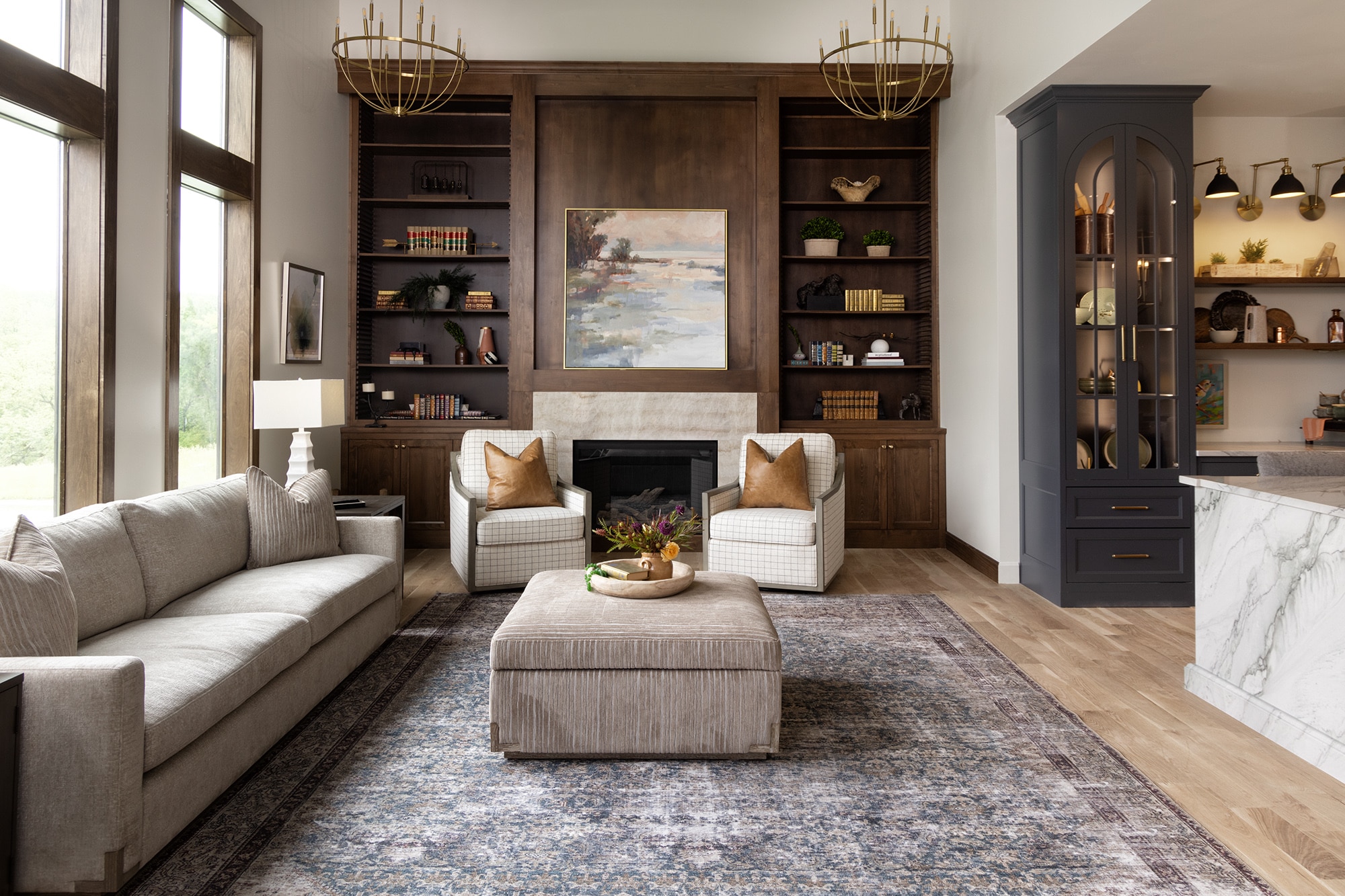 Living room with white couch, wood accent wall with fireplace, two large windows, and the fireplace using a beige marble look quartzite slab as a lining..