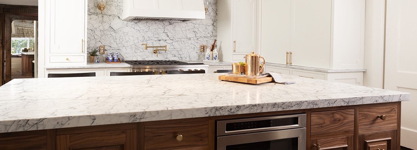 Kitchen with center island, white marble countertops and backsplash, and wood cabinets.