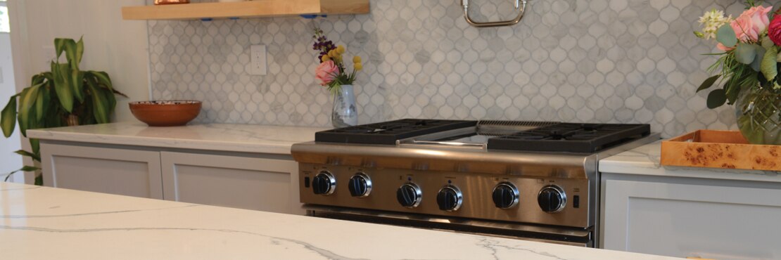 Remodeled kitchen with white with gray veining quartz countertops & island, gray marble mosaic backsplash, stainless steel gas stove/oven.