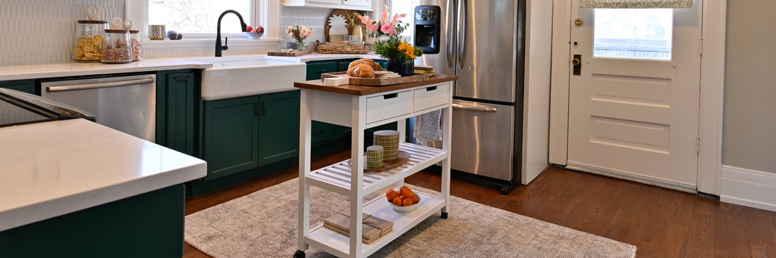 Farm house kitchen with white picket tile backsplash, white quartz countertops, large farm sink, butcher block island, dark green lower & white upper cabinets.