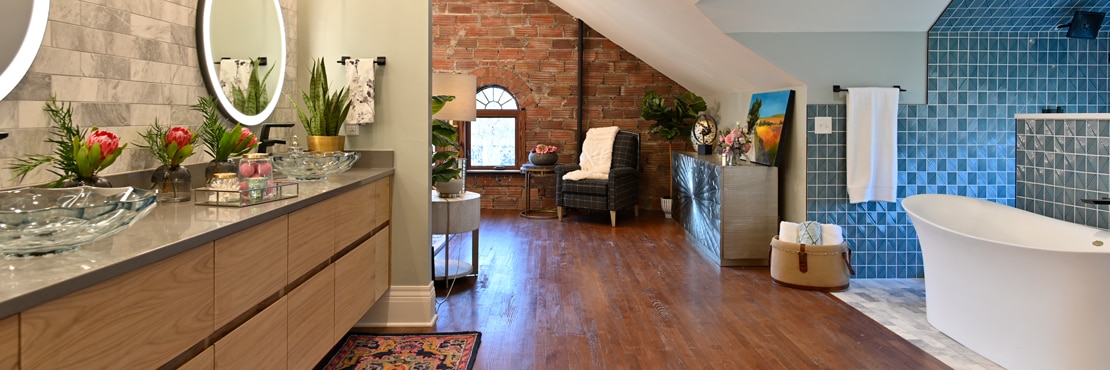 Renovated bathroom vanity with gray marble tile backsplash, gray quartz countertop, free-standing bathtub in front of shower with blue geometric tile.