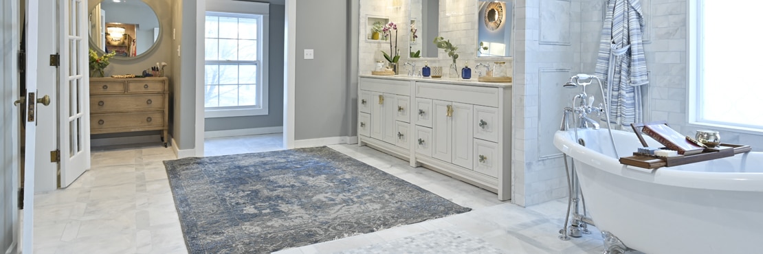 Bathroom with gray marble wall tile and floor tile, free-standing bathtub, vanity with white cabinets and marble framed mirrors.