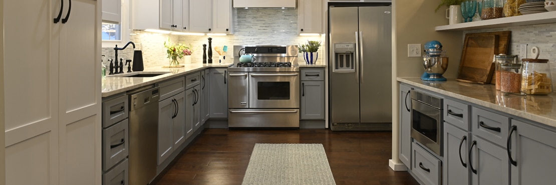 Remodeled kitchen with gray lower cabinets, lighted white upper cabinets, gray marble mosaic backsplash, tan quartzite countertops, and stainless steel appliances.