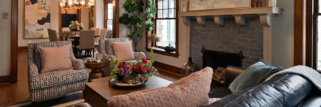 Cozy living room with black leather couch facing coffee table and two black & white chairs, and fireplace with blue-gray glass tile hearth and surround.