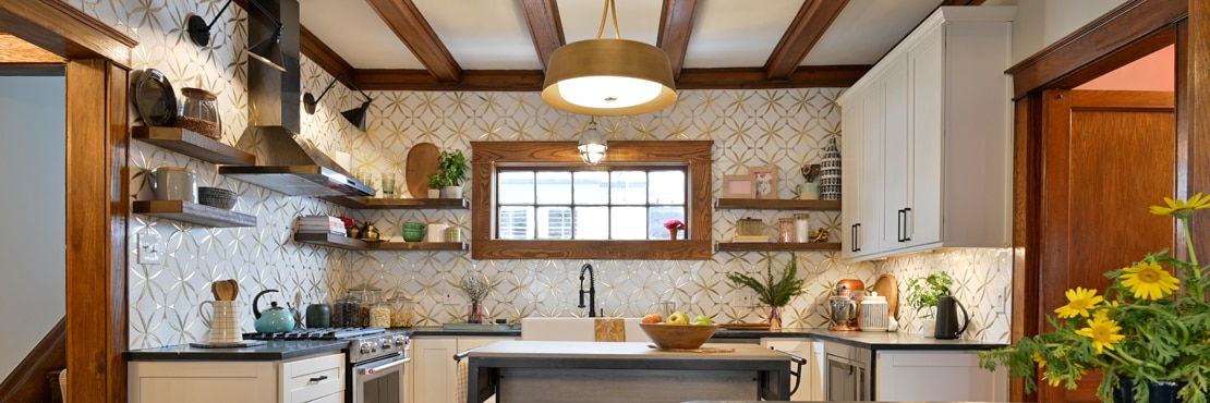 Farm house kitchen with white marble mosaic with embedded brass wall tile backsplash, black soapstone countertops, farm sink, and wood beams.
