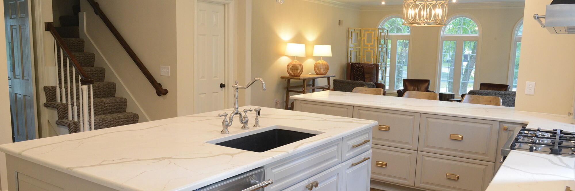 Remodeled kitchen with white with gray veining quartz countertops & island with built-in black under mount sink, polish silver faucet, and white cabinets.