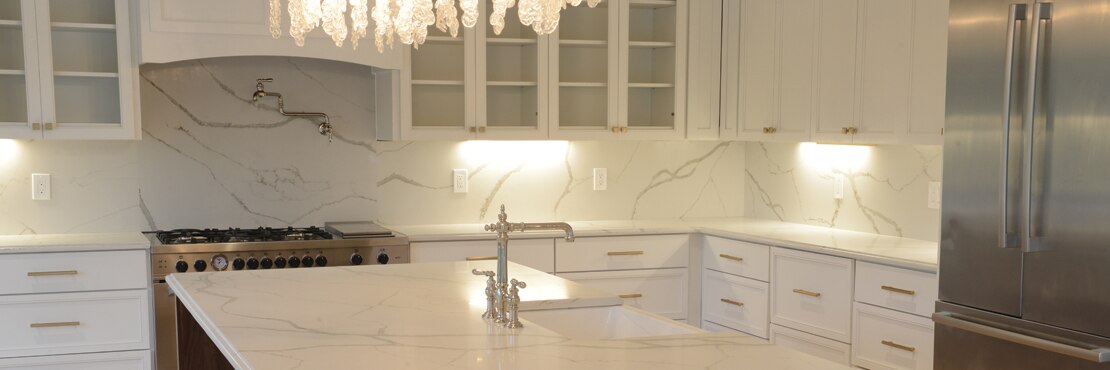 Kitchen with white cabinetry, white marble-look quartz countertops, island, and backsplash, large farmhouse sink.