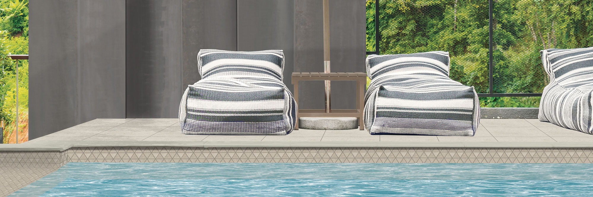 Outdoor pool with beige diamond mosaic pool tile, pool deck of beige stone look porcelain pavers, lounge chairs with white & gray striped covering.